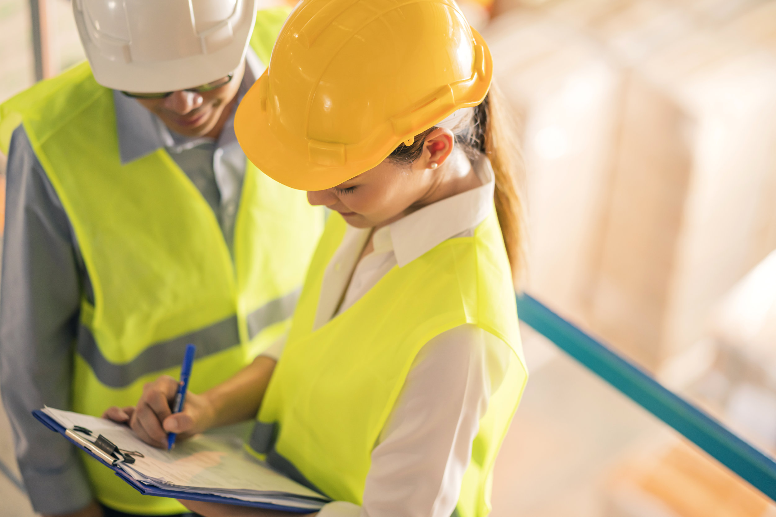 Two workers in high-visibility vests and hard hats conducting an inspection, with one writing on a clipboard.