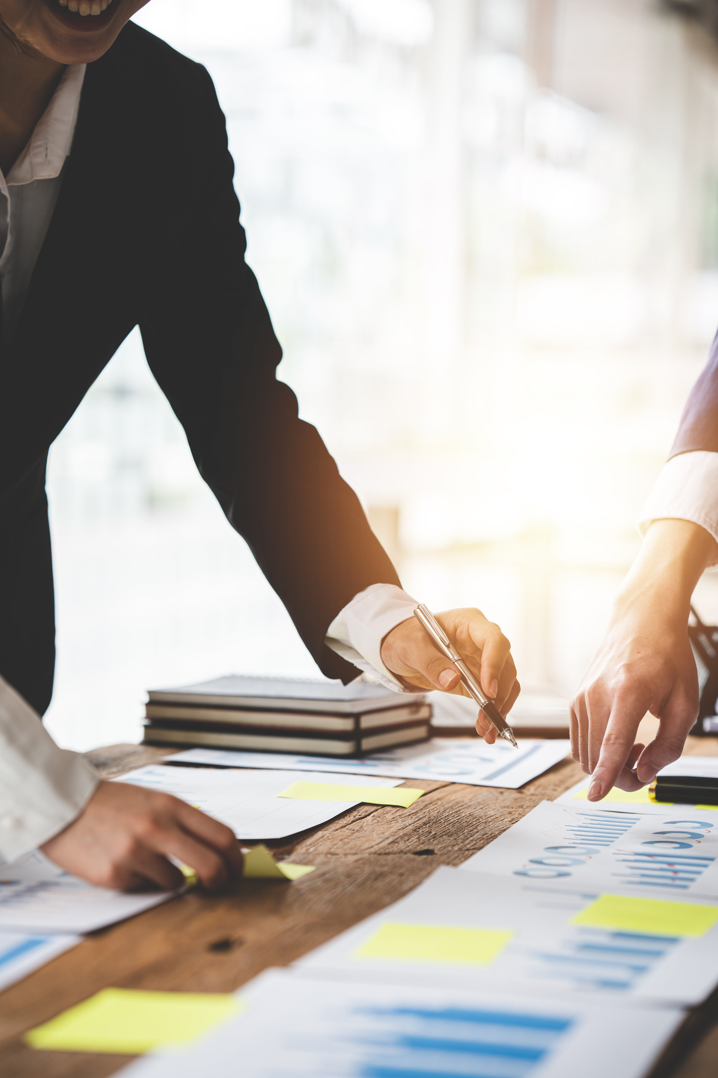 Business professionals collaborating on a project, examining documents with charts and graphs on a wooden table in a well-lit office.