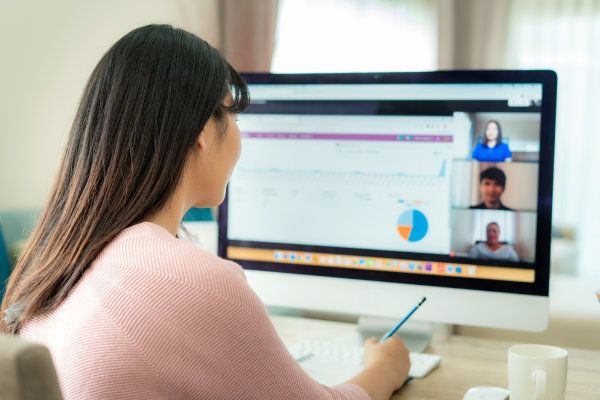 Business professional participating in a virtual meeting, viewing charts and graphs on a computer screen with colleagues visible in video call windows.